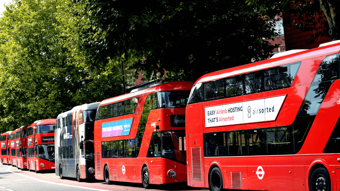 London red buses lined up on the road with adverts on their side.
