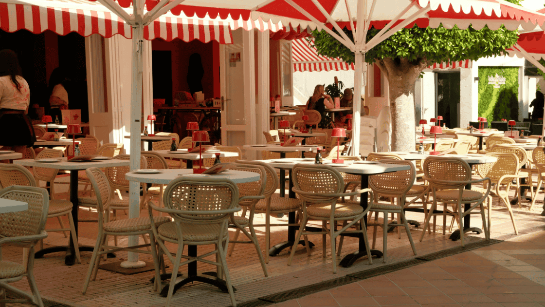 Sunny cafe with tables and chairs and a red and white striped awning